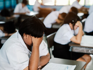 Students reading exam answer sheets exercises in classroom of school with headache and stress
