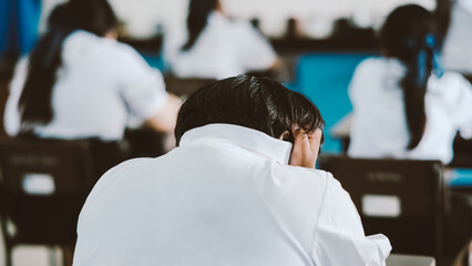Back of students reading exam answer sheets exercises in classroom of school with headache and stress