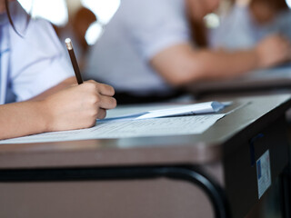 Close up hand of student reading and writing exam answer sheets exercises with stress in classroom