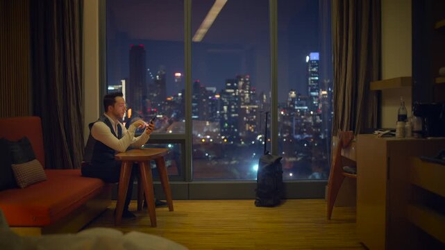 A businessman enjoys the beautiful city view at night from his modern, luxurious hotel room