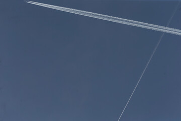 contrails create x, diagonal contrails create striking x shape, layered vapor trails converge in bold x pattern, aerial view capturing crisscrossed contrails forming prominent x against muted blue sky