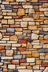 Fototapeta premium a rustic stone wall featuring an irregular, multicolored pattern of roughly rectangular and irregularly shaped stones in shades of beige, brown, gray, and red.