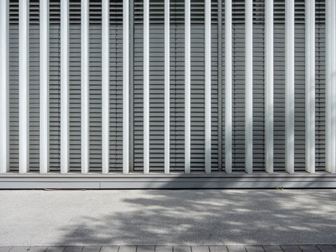 Modern architectural facade with vertical metal beams and horizontal blinds casting soft shadows on the ground