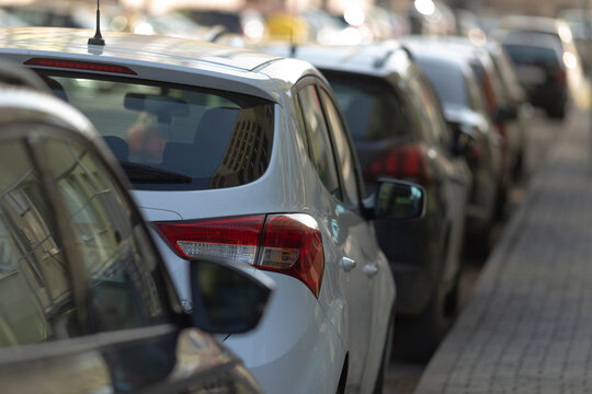 parked cars on busy street, vehicles lined up on crowded urban street, numerous parked vehicles along bustling city curbside, row of different cars parked tightly on busy city street with reflections