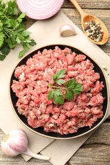 Raw minced meat with parsley and spices on wooden table, flat lay