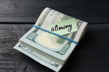 Note with word Alimony and money on wooden table, closeup