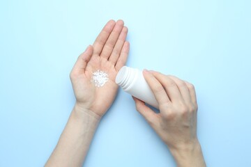 Woman with bottle of talcum powder on light blue background, top view