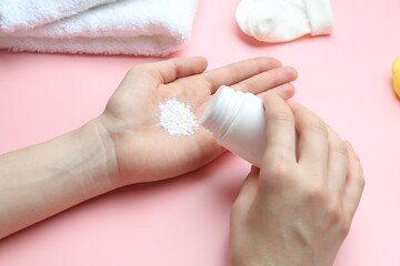 Woman with bottle of talcum powder and baby accessories on pink background, closeup