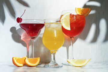 Glasses of tasty cocktails with garnish on white marble table