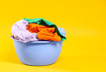 Plastic basin with laundry on yellow background. Space for text