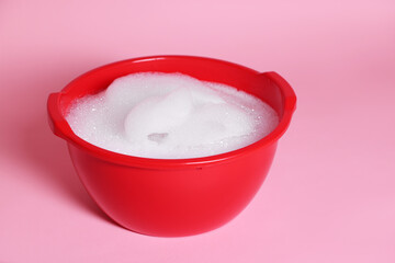Red plastic basin with soapy water on pink background, closeup