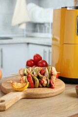 Tasty skewers with chicken, vegetables and air fryer on wooden table indoors, closeup