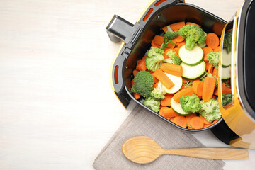 Raw carrots, broccoli and zucchini in air fryer on white wooden table, top view. Space for text