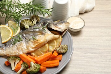 Cooked fish served with rosemary, lemon and vegetables on wooden table, closeup. Space for text