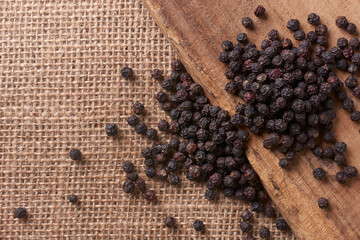 black peppercorns scattered on wooden plank and burlap fabric, rustic textures with copy space for text, concepts of culinary spice and natural ingredients, close-up macro view
