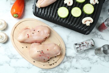 Electric grill with zucchini, mushrooms and raw chicken breasts on white marble table, flat lay