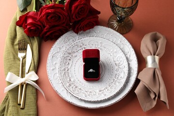 Beautiful table setting for romantic dinner, box with engagement ring and roses on color background