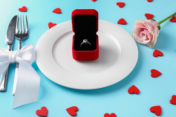 Beautiful table setting for romantic dinner, box with engagement ring and rose on light blue background, closeup