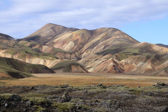 A stunning panoramic view of multicolored volcanic mountains, showcasing rich hues of brown, orange, and green shaped by mineral deposits