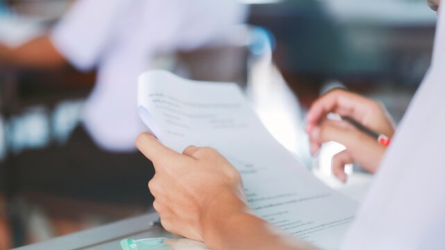 Students writing and reading exam answer sheets exercises in classroom of school with stress