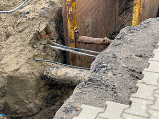 Open construction trench exposing utility pipes and electrical cables, secured by metal shoring for...