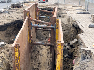 Busy urban construction site with a deep excavated trench, securely supported by a heavy-duty metal...