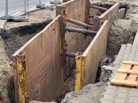 Deep urban construction trench supported by a heavy-duty metal shoring system with hydraulic braces for safe excavation and utility infrastructure installation