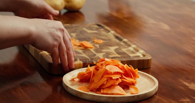 A chef arranges sliced fresh carrots on a wooden board on a table, preparing ingredients for a healthy vegan dish, home cooking process, natural food, country kitchen atmosphere, healthy lifestyle