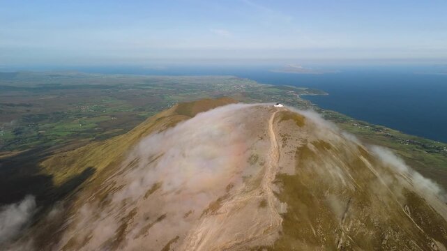 Amazing 4K aerial video of flying above and around Most Famous mountain in Ireland - Croagh Patrick in windy weather, with moving fog and clouds with breathtaking views around, Westport, Ireland
