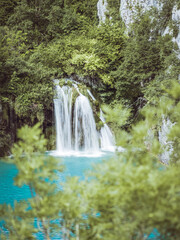 Fototapeta premium Beautiful view of a cascading waterfall flowing into a turquoise lake surrounded by lush green forest in Plitvice Lakes National Park, Croatia.