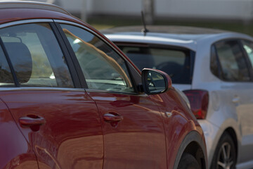 red car beside white car parking creating contrast and color dialogue, side mirrors and door lines align while reflections and shadows add depth; everyday lot scene suggests choice and comparison