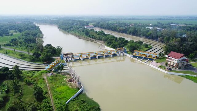 Aerial drone shot of the Rentang Dam/Weir in Majalengka, Indonesia. It shows the structure, including the sluice gates, water channels, and surrounding green areas.