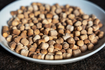 A close-up shot of a white bowl filled with small, light-brown, dried food - a traditional snack smoked kurut (kurt) - dried sour milk cheese (dried curd cheese). 