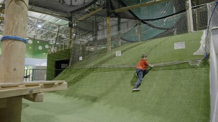 Child sliding down artificial turf hill in indoor playground. Creative