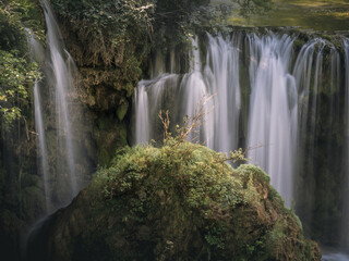 Obraz premium Close view of multiple waterfalls dropping over a mossy cliff around a rocky outcrop, with lush vegetation in Rastoke, Croatia.