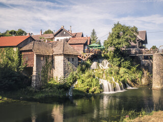 Obraz premium Traditional watermill houses beside cascading waterfalls in the village of Rastoke, Croatia, where historic architecture meets lush greenery.