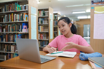 School student girl having video call on her computer in library at school.