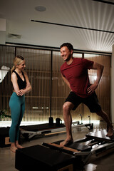 Fitness instructor guides a man through a pilates session at a modern studio during morning hours,...