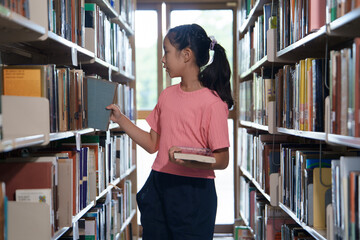 A elementary school girl is reading and select a book in the library.