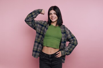 Smiling young woman showing strength with a confident pose against a pink background in a casual...