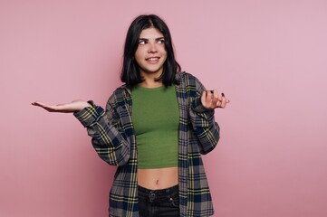 Young woman in casual outfit posing against pink background with playful expression and confident...
