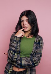Young woman in casual outfit poses with playful expression against a soft pink backdrop while...