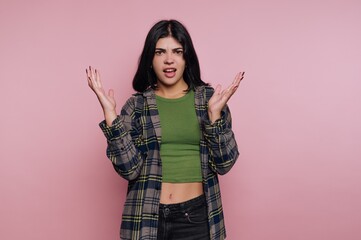 Young woman expresses confusion and frustration against a pink background in a casual outfit