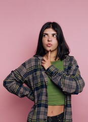 Fototapeta premium Young woman ponders thoughtfully in a cozy plaid shirt against a pink background