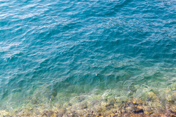 Obraz premium Clear turquoise sea meets a rocky shore, with gentle waves and sunlit ripples