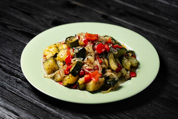 healthy vegetarian dish made of roasted zucchini, potatoes, red peppers and onions, served on a light green plate. Nutritious homemade