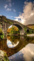 Stone bridge arched over river reflecting autumn landscape