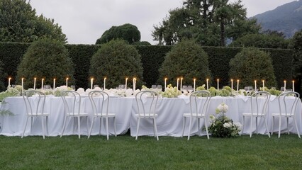 Elegant white wedding reception table setup in garden at dusk. Action