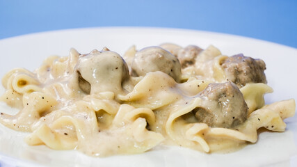 Swedish meatballs with creamy sauce served on a white plate against a blue background