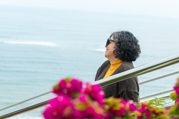 A woman is sitting on a railing overlooking the ocean